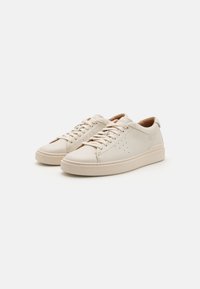 Beige leather sneakers with a smooth texture, round toe, and perforated detailing on the side. Features flat laces and a cushioned footbed.