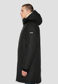 Schwarzer isolierter Parka mit Kapuze, ausgestattet mit einem Reißverschluss vorne, Fleece-Futter und Logo-Aufnäher am Ärmel. Glatte, matte Oberfläche.