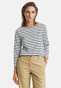 Langsleeve, marineblauw en wit gestreept katoenen t-shirt met een ronde hals en een klein geborduurd logo. Gepaard met beige broeken.