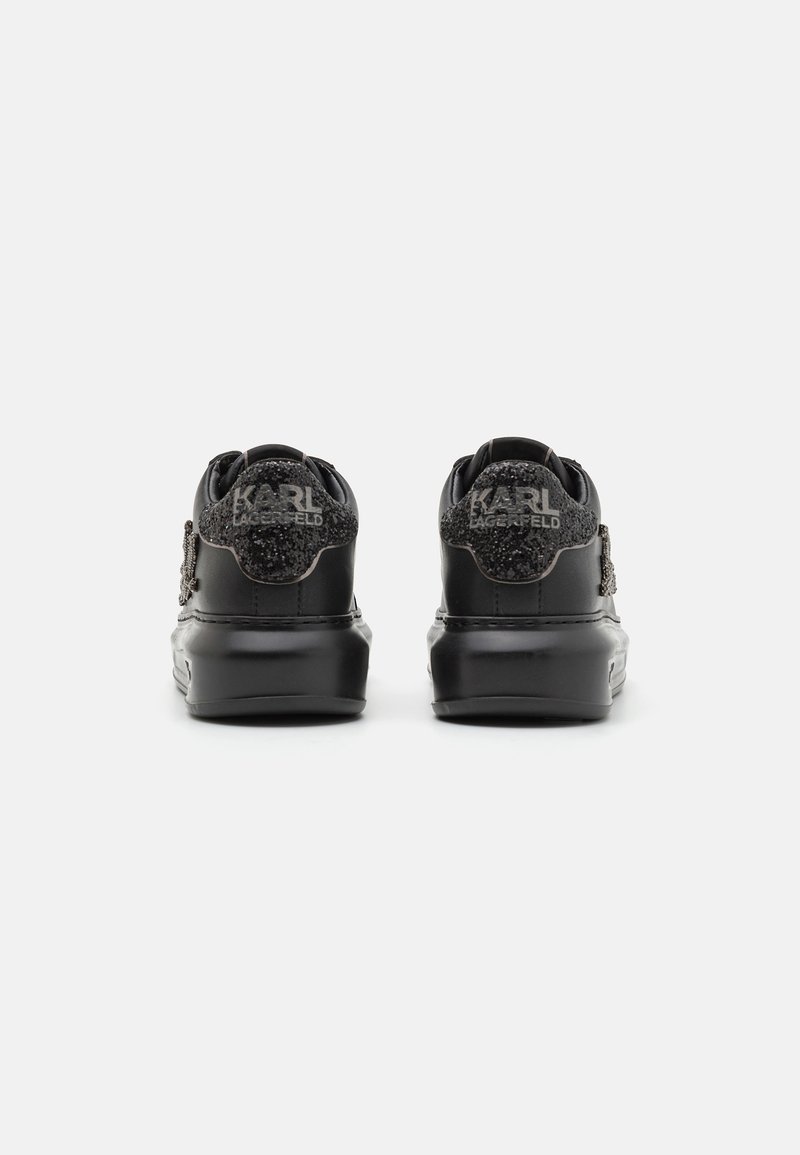 Une paire de baskets noires avec des patches de talon texturés pailletés arborant le logo "KARL LAGERFELD", présentée de dos sur un fond blanc.