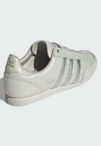 Gaiši zaļas ādas sporta kurpes ar sudraba svītrām, perforētu purngalu un teksturētu zolī. Uz papēža ir Adidas logotips un detalizēts uzraksts "Japan".