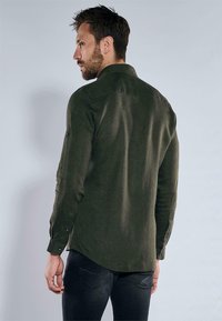 Grünes Langarmhemd aus strukturiertem Stoff, mit klassischem Kragen, Knopfmanschetten und abgerundetem Saum, von hinten gezeigt.