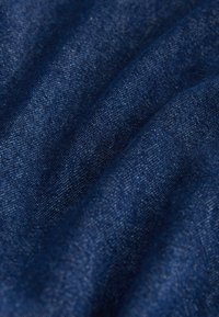 Tissu denim bleu foncé avec une texture de tissage visible, présenté en plis doux qui mettent en valeur l'épaisseur du matériau et sa surface irrégulière.