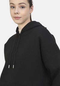 Sudadera negra fabricada en un tejido suave, que cuenta con una capucha forrada, cordones con extremos metálicos y un corte holgado.
