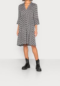 Robe à motifs noir et blanc avec un décolleté en V, des manches cloche trois-quarts et une jupe évasée, assortie à des bottes de cheville noires à semelle épaisse.