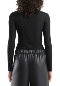 Czarny prążkowany top z długim rękawem o dopasowanym kroju, zestawiony z czarnymi spodnimi ze sztucznej skóry z wysokim stanem i elastycznym pasem.