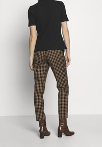 Svart kortärmad topp i kombination med bruna rutig byxor. Byxorna har en smal passform och texturen ser slät ut med en subtil lyster.