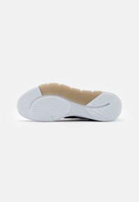 Suola di una sneaker Adidas bianca e nera con battistrada in gomma testurizzata bianca e beige e logo Adidas vicino all'arco su uno sfondo bianco uniforme.
