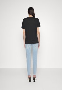 Camiseta negra de manga corta exhibida en un modelo, combinada con jeans ajustados de color azul claro y zapatos de tacón negro con acentos de borlas.