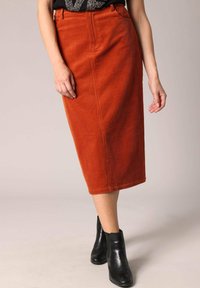 Jupe midi en velours côtelé orange rouillé avec des côtes verticales, dotée d'une taille ajustée et de deux poches latérales, associée à des bottines noires.