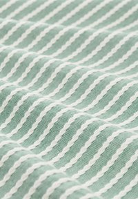 Grün gestreifter Stoff mit dünnen weißen Wellenlinien. Das Material hat eine strukturierte Oberfläche, die eine weiche und gemusterte Erscheinung schafft.