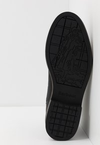 Sola de sapato de borracha preta com padrão de grip texturizado. Apresenta logotipo em relevo e detalhe de design. Bordas suaves com uma forma ligeiramente curvada.