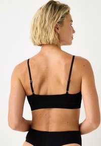 Svart bralette med tunna justerbara band, texturerat tyg och en sömlös design som erbjuder en minimalistisk och funktionell stil.