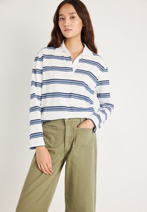 Polo de manga larga blanco con rayas horizontales azules y cuello. Combinado con pantalones de pierna ancha verde oliva con bolsillos delanteros.