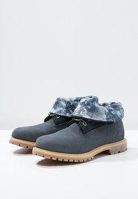 Paire de bottines bleu marine avec semelles à crampons marron clair et poignets rabattus à motif tie-dye bleu-gris.