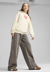 Sudadera beige con un diseño de llamas en la parte frontal, combinada con pantalones grises holgados. El conjunto se completa con zapatillas sin cordones en tonos marrón y crema.