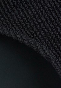 Svart tyg med en strukturerad, ögla-mönster på ena kanten, i kontrast med det släta svarta materialet under. Den övergripande designen är minimalisk.