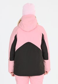 Rosa und schwarze isolierte Winterjacke mit Kapuze, die ein Farbblockdesign und eine glatte Textur aufweist. Tragen mit einer rosa Mütze.