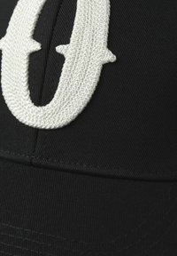 Zwarte pet met een verhoogd, tekstuurlijk wit geborduurd logo. Het materiaal lijkt stevig met zichtbare stiksels en een gebogen klep.