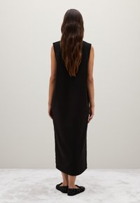 Schwarzes ärmelloses Kleid mit lockerer Passform, knielang, aus weichem Stoff. Trägt dazu strukturierte schwarze Schuhe. Einfaches, minimalistisches Design.