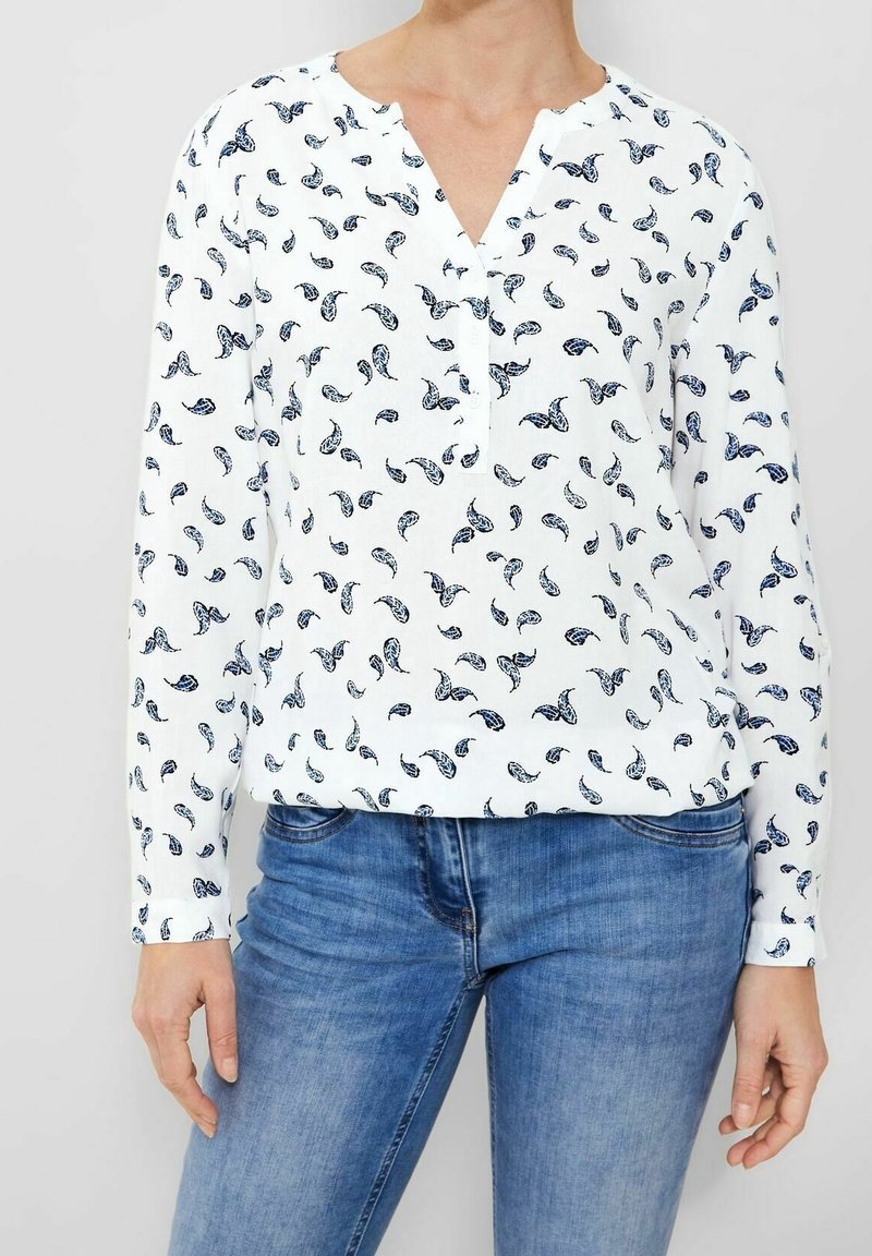 Hvid skjorte med lange ærmer og marineblå paisley-mønstre, V-halskrave, parret med medium-vasket blå denim jeans.