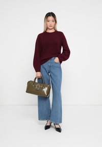 Burgundy kötött pulóver, kék bővülő nadrág, olívzöld táska csillag díszítéssel és fekete hegyes orrú balerina cipők. Egyszerű és modern ruházat.