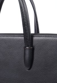 Sort læder håndtaske med struktureret overflade, dobbelte håndtag og sølvfarvet hardware detalje nær bunden af håndtagene.