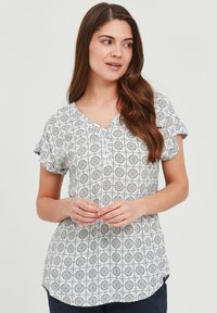 Rövid ujjú, V nyakú blúz könnyű anyagból; fehér alapon fekete geometrikus virágmintával, ívelt szegéllyel.