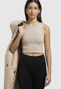 Beige cropped tanktop met een gladde textuur, gecombineerd met hoge zwarte leggings. Een beige jack hangt over één schouder.