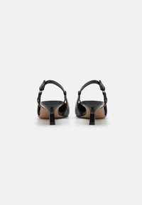 Black leather heeled sandals with a rounded toe, adjustable ankle strap, and a small block heel. Smooth texture and minimalist design.