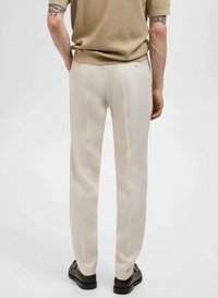 Beige op maat gemaakte broeken met een gladde textuur, rechte snit, subtiele plooien en twee achterzakken, gedragen met een geribbelde bruine top.