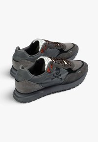 Zapatillas grises que combinan malla y ante, con un diseño estampado, detalles en color naranja y un emblema de calavera y tibias cruzadas en el lateral.