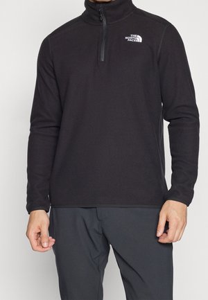 Mężczyzna noszący czarny polar North Face z zamkiem na ćwiartkę i długimi rękawami, w połączeniu z ciemnymi spodniami.