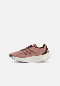Baskets de sport rose clair avec dessus en maille, accents marron et semelle texturée blanche. Elles présentent une forme allongée et des découpes élégantes pour la ventilation.