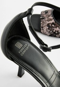Escarpin en cuir noir avec une bride ajustable, featuring un accent en sequins sur le dessus. Logo "Forever Comfort" sur la semelle intérieure.