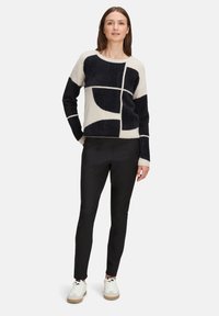 Crème en marine gestreepte trui met geometrische ontwerpen, zachte textuur, lange mouwen, gecombineerd met zwarte tapered broek en witte sneakers.