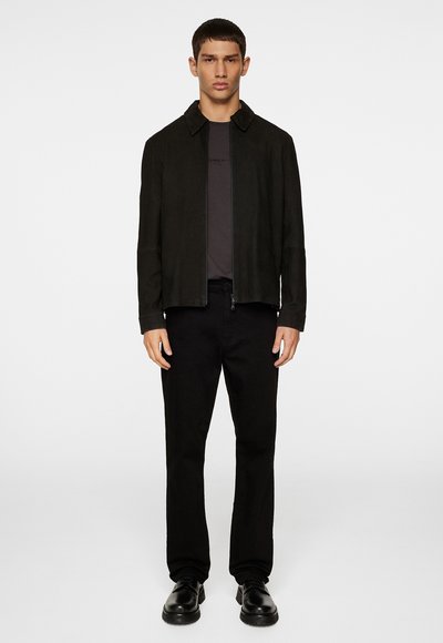 Zwart suède jasje met een staande kraag, gedragen over een donkergrijze shirt en zwarte broek, met een ritsluiting en een slanke snit.