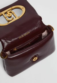 Borsa in pelle bordeaux con accessori dorati, caratterizzata da un design ritagliato e una tasca interna con zip. Logo impresso sul davanti.