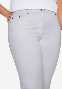 Jeans gris clair en matière extensible, avec une coupe slim, une fermeture éclair et des accents en métal sur les poches.