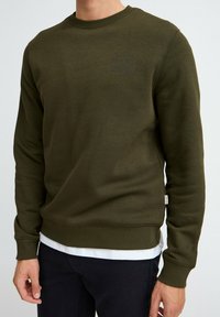 Olijfgroene crewneck sweatshirt van zachte stof, met een geribbelde halslijn, boorden en zoom, en subtiele tekstdetails op de borst.