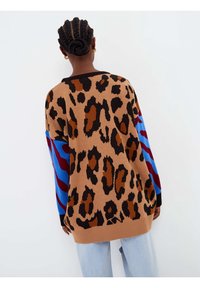 Pull en tricot imprimé léopard avec taches marron, noires et orange; manches rayées contrastantes bleu et rouge; encolure ronde; coupe décontractée.