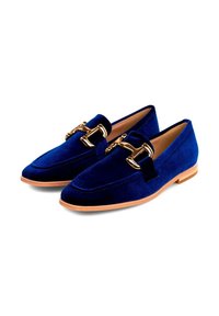 Un paio di mocassini in velluto blu con dettagli in oro a forma di morso e suole in legno marrone chiaro, mostrati su sfondo bianco.
