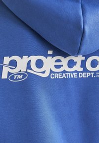 Sudadera azul con una textura suave, que presenta una gran impresión gráfica blanca que dice "project" y "CREATIVE DEPT." cerca de la capucha.