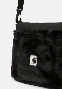 Čierna crossbody taška s mäkkým umelým kožušinovým povrchom, hladkým nylonovým vrchom, zipsovým uzáverom a viditeľnou nášivkou loga na prednej strane.