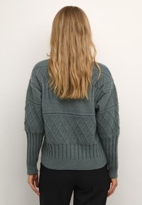 Textured, knitted sweater in dark green with diamond and ribbed patterns. Loose fit with long sleeves and a round neckline.