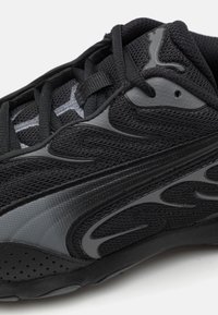 Chaussure de sport noire avec un dessus en mesh et des accents texturés, un design courbé et des détails tonaux sur les côtés. Semelle extérieure texturée avec des perforations.