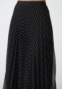 Gonna nera plissettata con pois argentati, caratterizzata da un design fluido e una texture trasparente, rifinita con una vita aderente.