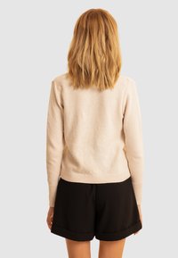 Maglione a maglia rosa chiaro con un motivo testurizzato, dotato di maniche lunghe e orlo a coste, abbinato a pantaloncini neri.