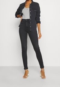 Vaqueros de mezclilla negra de cintura alta combinados con una camiseta gris y una camisa de mezclilla oscura, complementados con sandalias de tacón bloque blanco.