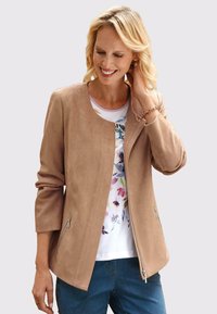 Beige faux suede jacket met een ronde hals, ritszakken aan de zijkant en driekwart mouwen, over een bloemenhemd.